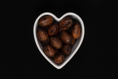 Siyah arka planda kalp şeklinde bir kasede ceviz kabuğu olan fındık..