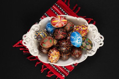 Geleneksel Doğu Avrupa tarzında boyanmış Paskalya yumurtaları, siyah bir arka planda izole edilmiş bir kasede çiçek / geometrik bir tasarım ile..