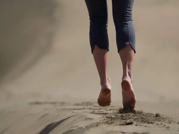 Bara fötter av ung kvinna jogging/promenad på stranden i soluppgången — Stockfoto