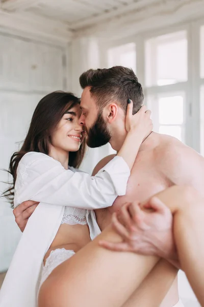 Genç mutlu çift evde, sarılma ve öpüşme vardır. Sevilen olanlar pijama deli ve gülmek güzel güneşli sabah.