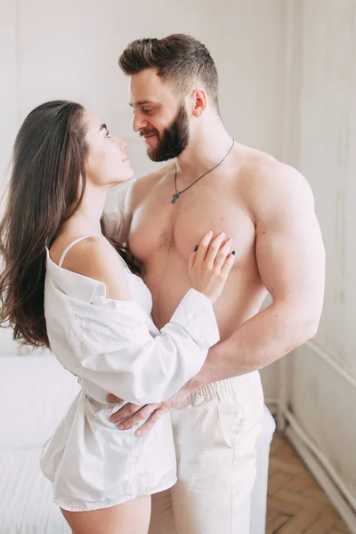 Genç mutlu çift evde, sarılma ve öpüşme vardır. Sevilen olanlar pijama deli ve gülmek güzel güneşli sabah.