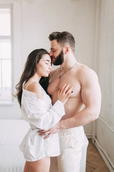 Genç mutlu çift evde, sarılma ve öpüşme vardır. Sevilen olanlar pijama deli ve gülmek güzel güneşli sabah.