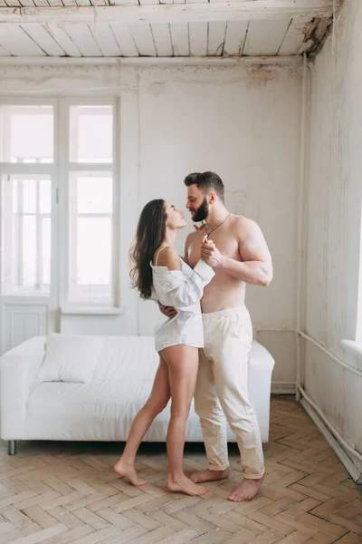 Genç mutlu çift evde, sarılma ve öpüşme vardır. Sevilen olanlar pijama deli ve gülmek güzel güneşli sabah.