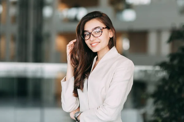 Beautiful Russian business girl with glasses, standing with arms crossed and smiling. Office style and business image, business meeting and greeting