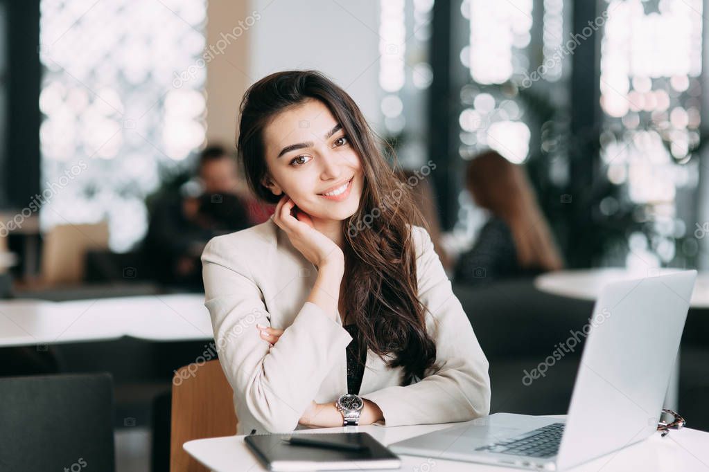 Beautiful Russian business girl working on laptop, smiling and typing on the keyboard. Working time, business image and a job in a cafe