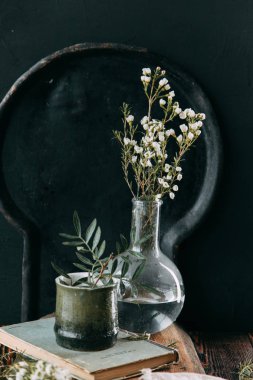 Bahar çiçekleri ve yeşillik dekor cam şişe su ve camına damlacıkları ile tablo içinde. Sıcak gama ve küçük çiçekler ve çim, koyu ahşap arka plan ile ölçülü kompozisyon