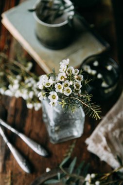 Bahar çiçekleri ve yeşillik dekor cam şişe su ve camına damlacıkları ile tablo içinde. Sıcak gama ve küçük çiçekler ve çim, koyu ahşap arka plan ile ölçülü kompozisyon