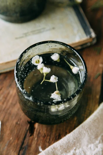 Bahar çiçekleri ve yeşillik dekor cam şişe su ve camına damlacıkları ile tablo içinde. Sıcak gama ve küçük çiçekler ve çim, koyu ahşap arka plan ile ölçülü kompozisyon
