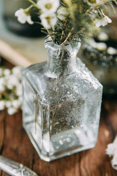 Bahar çiçekleri ve yeşillik dekor cam şişe su ve camına damlacıkları ile tablo içinde. Sıcak gama ve küçük çiçekler ve çim, koyu ahşap arka plan ile ölçülü kompozisyon