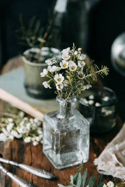 Bahar çiçekleri ve yeşillik dekor cam şişe su ve camına damlacıkları ile tablo içinde. Sıcak gama ve küçük çiçekler ve çim, koyu ahşap arka plan ile ölçülü kompozisyon
