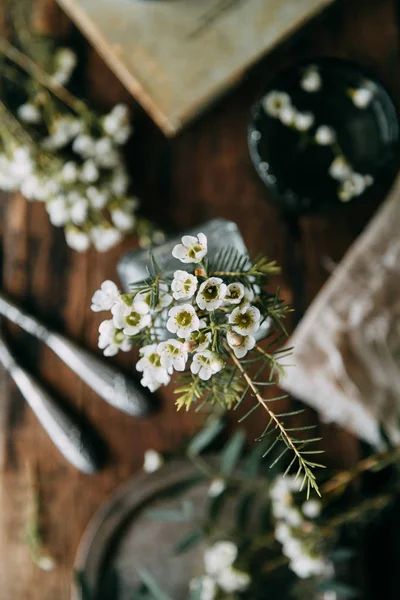 Bahar çiçekleri ve yeşillik dekor cam şişe su ve camına damlacıkları ile tablo içinde. Sıcak gama ve küçük çiçekler ve çim, koyu ahşap arka plan ile ölçülü kompozisyon