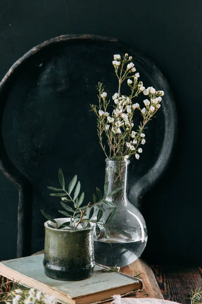 Bahar çiçekleri ve yeşillik dekor cam şişe su ve camına damlacıkları ile tablo içinde. Sıcak gama ve küçük çiçekler ve çim, koyu ahşap arka plan ile ölçülü kompozisyon