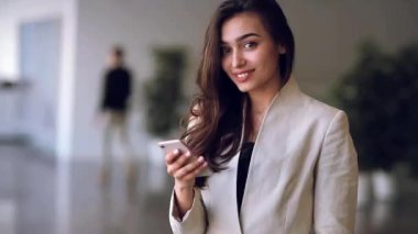Gülümseyen güzel Rus iş kız elleri, bir telefon. Office stili, katı giyim ve etkileyici bir görünüm. Telefon görünüyor ve gülüyor