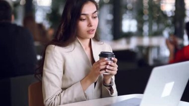 Holding ve kahve içme bir dizüstü bilgisayar üzerinde çalışan iş kız. Serbest meslek restoranda, başarılı kadın. Office durum, mutlu başarı ve güzel bir görünüm.
