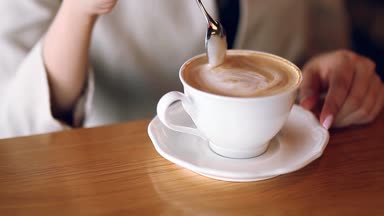 Kahve, bir kafede oturan kızla ve köpük karışımları. Bir kaşık ve içecek kahve tutar. Kapuçino köpük, daha sıcak ve tatmin edici. Sabah canlandırıcı içki