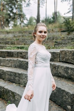 Doğada Avrupa tarzında düğün. Taş bir merdivende beyaz elbiseli bir gelin.. 