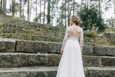 Doğada Avrupa tarzında düğün. Taş bir merdivende beyaz elbiseli bir gelin.. 