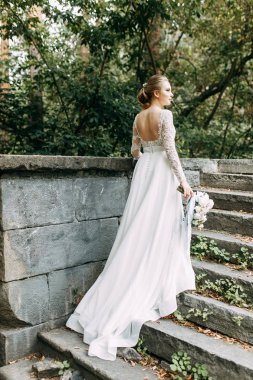 Doğada Avrupa tarzında düğün. Taş bir merdivende beyaz elbiseli bir gelin.. 