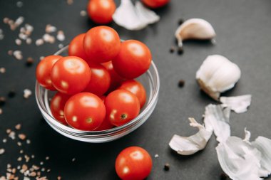 Siyah arka plandaki malzemeler. Sarımsaklı kiraz domatesleri ve kasede tuz.. 