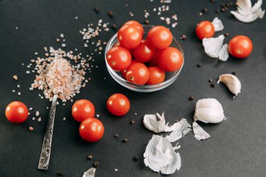 Siyah arka plandaki malzemeler. Sarımsaklı kiraz domatesleri ve kasede tuz.. 