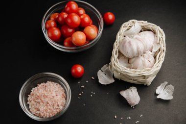 Siyah arka plandaki malzemeler. Sarımsaklı kiraz domatesleri ve kasede tuz.. 