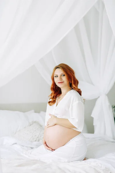 幸せな赤ん坊を待っている 白いベッドの上の妊婦 — ストック写真