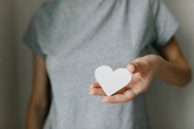 Kızın üzerinde gri tişört var. Kağıt beyaz kalp, ilaç. Bir kadının çapraz kollarından bir kalp.. 