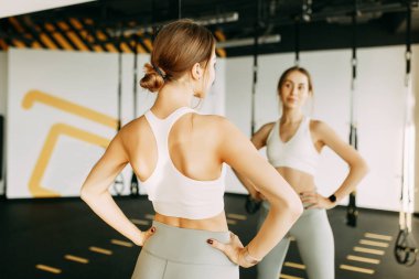 she Looks at herself. Portrait of a sports girl in the gym. Beautiful white girl in the mirror reflection. 