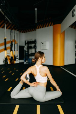 Flexibility exercises on a black background. Stretching in a dark room on a rug. Beautiful girl athlete on the floor. 