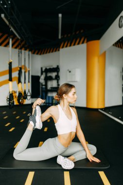 Flexibility exercises on a black background. Stretching in a dark room on a rug. Beautiful girl athlete on the floor. 