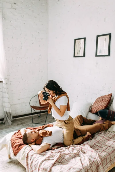 室内スタジオでのラブストーリー 彼らはカメラで互いを撃つ 女の子はベッドの上で男の写真を撮る — ストック写真