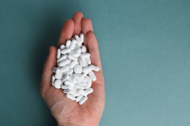 Mavi arka plandaki beyaz tabletler izole edilmiş. Tabletli bir el. Avuç içlerine bir yığın hap. Virüs koruması ve 2019-ncov. 