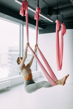 Exercises in the gym. Suspended in the air. Girl in a yoga hammock. Relax and grouped pose. 