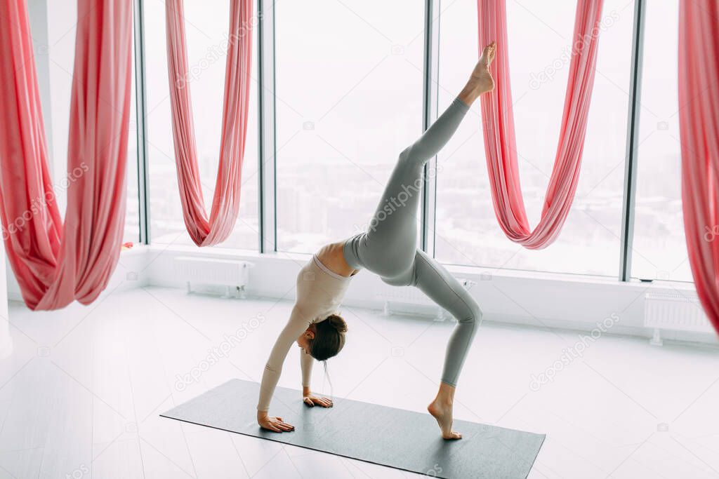 Beautiful girl athlete on the floor. Flexibility exercises on a light background. Stretching in a white room on a rug. 
