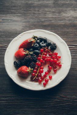 Koyu bir arka planda çilek, üzümler ve yabanmersini. Yaban mersinli tabak. 