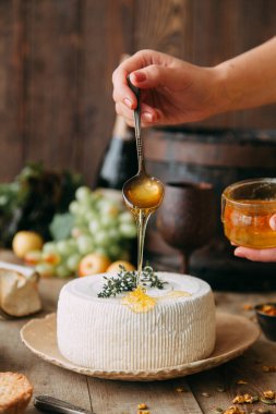  Tabakta büyük, yuvarlak bir peynir. Peynir balla sulanır. Şefin elleri peyniri hazırlar..