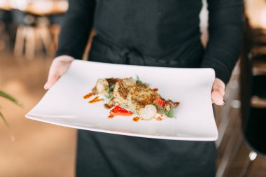 Beyaz tabakta et ve sebzeli sıcak yemek. Garson restoranda tabak taşır.. 