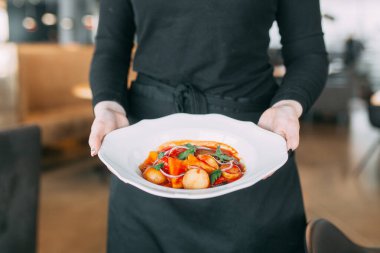 Beyaz tabakta et ve sebzeli sıcak yemek. Garson restoranda tabak taşır.. 