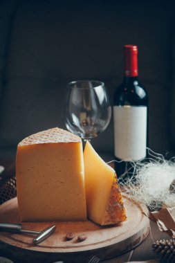 Koyu arkaplanda peynir ve şarap kompozisyonu. Bir dilim peynir ve bir bardak şarap. Büyük sert parmesan peyniri.. 