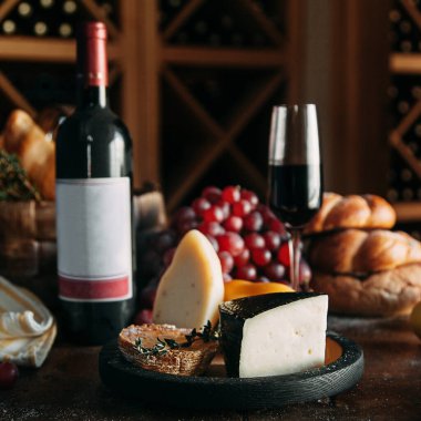 Bir dilim sert parmesan peyniri ve bir şişe şarap. Peynirli, şaraplı ve ekmekli kompozisyon. 