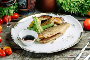 Ahşap arka planda sebze dekoru olan restoran yemeği. Soslu bir tabakta kızartılmış deniz balığı.. 