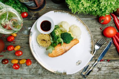 Ahşap arka planda sebze dekoru olan restoran yemeği. Soslu bir tabakta kızartılmış deniz balığı.. 