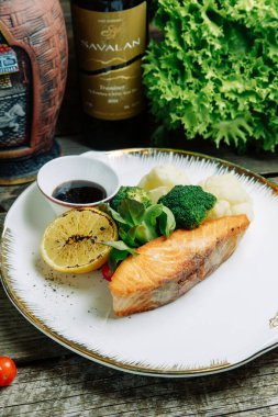 Ahşap arka planda sebze dekoru olan restoran yemeği. Soslu bir tabakta kızartılmış deniz balığı.. 