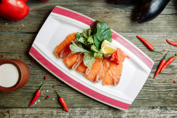 Restaurant dish with vegetable decor on a wooden background. Salted salmon cut into slices on a plate.