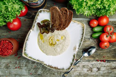 Ahşap arka planda sebze dekoru olan restoran yemeği. Mantarlı püre çorbası ve tabakta ekşi krema. 