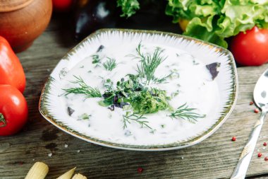 Ahşap arka planda sebzeli restoran yemeği. Azerbaycan Dovga çorbası. Tabakta yeşillikler var.. 