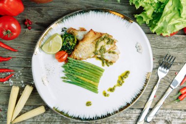 Ahşap arka planda sebze dekoru olan restoran yemeği. Soslu bir tabakta kızartılmış deniz balığı.. 