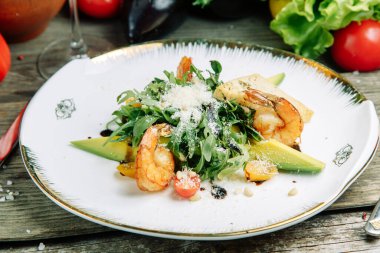  Ahşap arka planda sebzeli restoran yemeği. Karidesli salata, avokado ve roka..