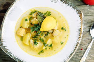 Ahşap arka planda sebzeli restoran yemeği. Tabakta balık, deniz ürünü ve limon çorbası.. 