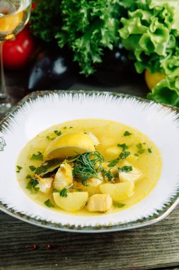 Ahşap arka planda sebzeli restoran yemeği. Tabakta balık, deniz ürünü ve limon çorbası.. 